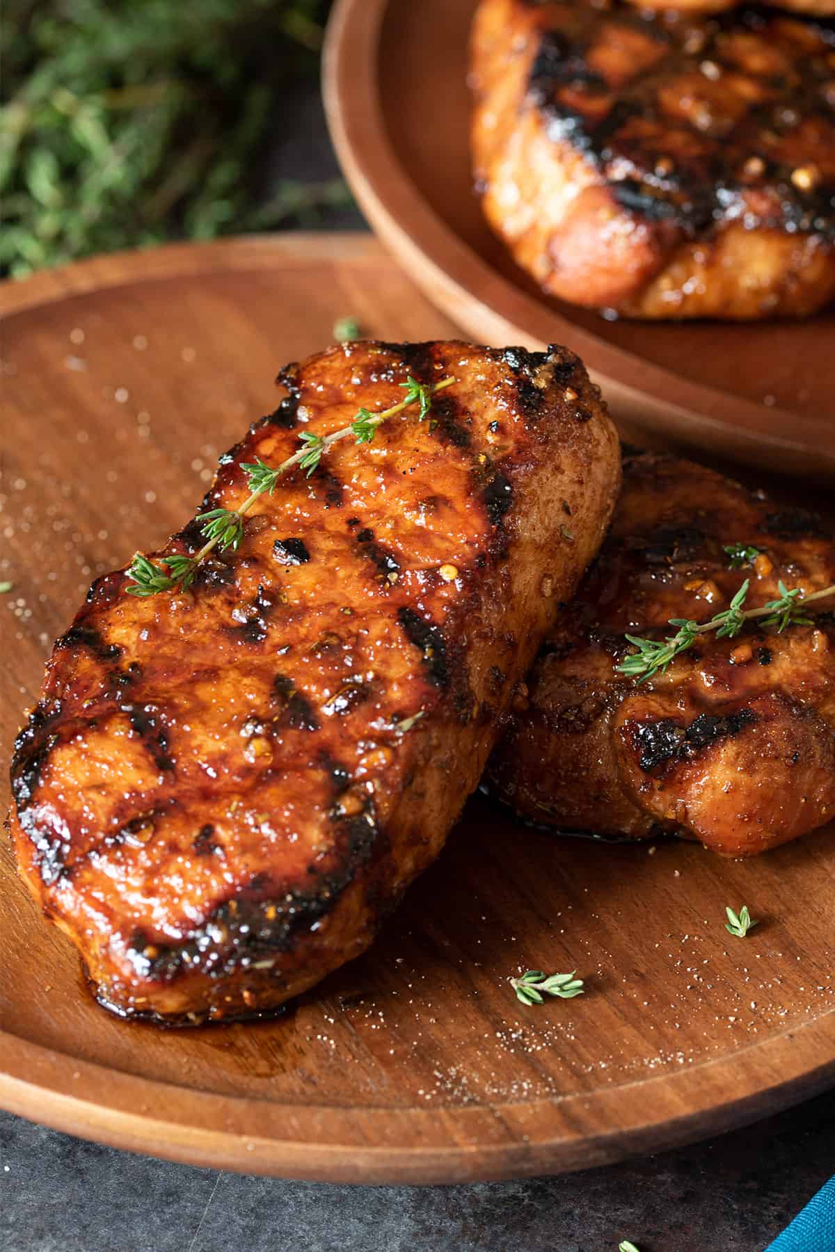 Two grilled pork chops with grill marks laid out on a wooden background.