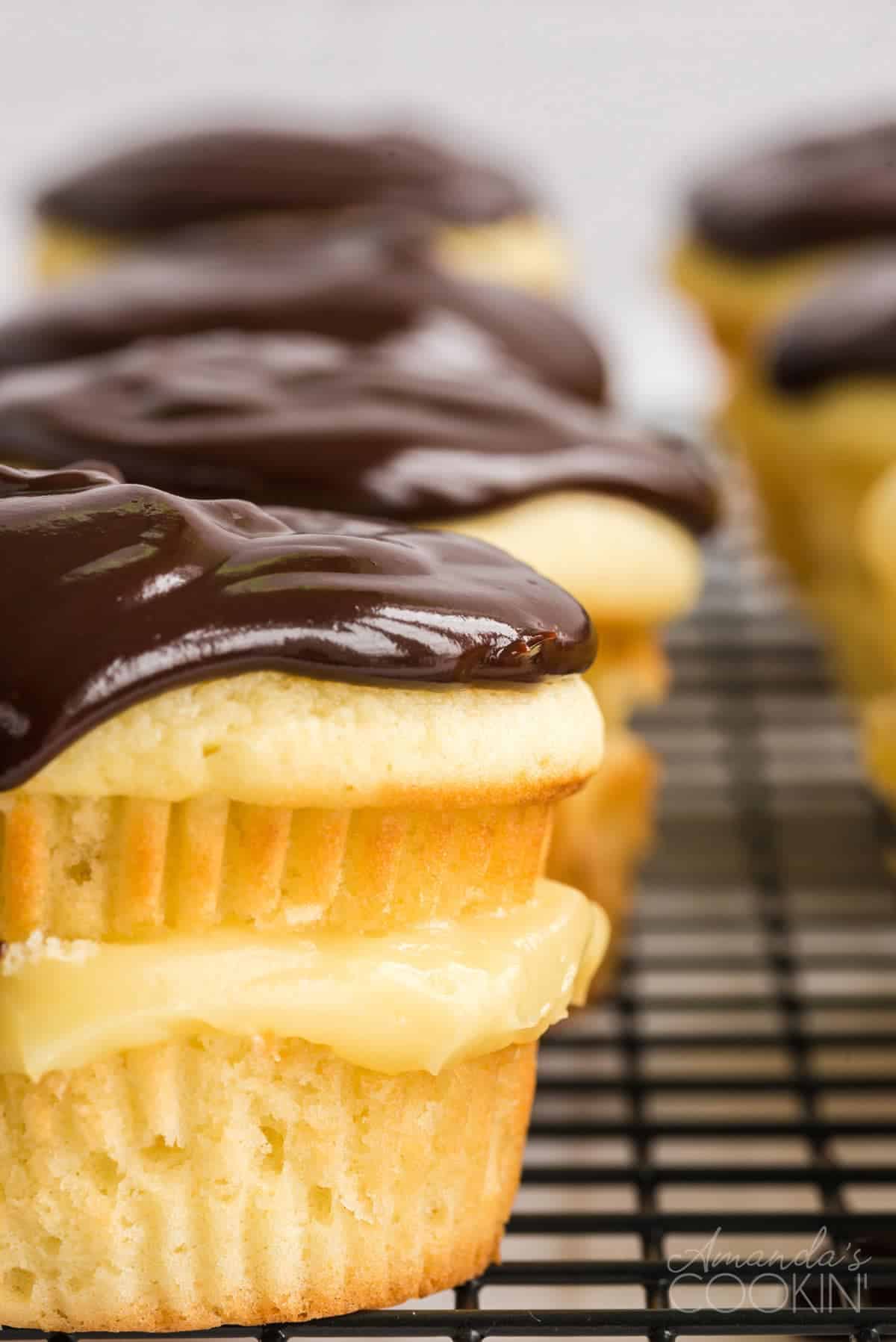 Boston Cream Pie style cupcake with chocolate ganache on wire baking rack.