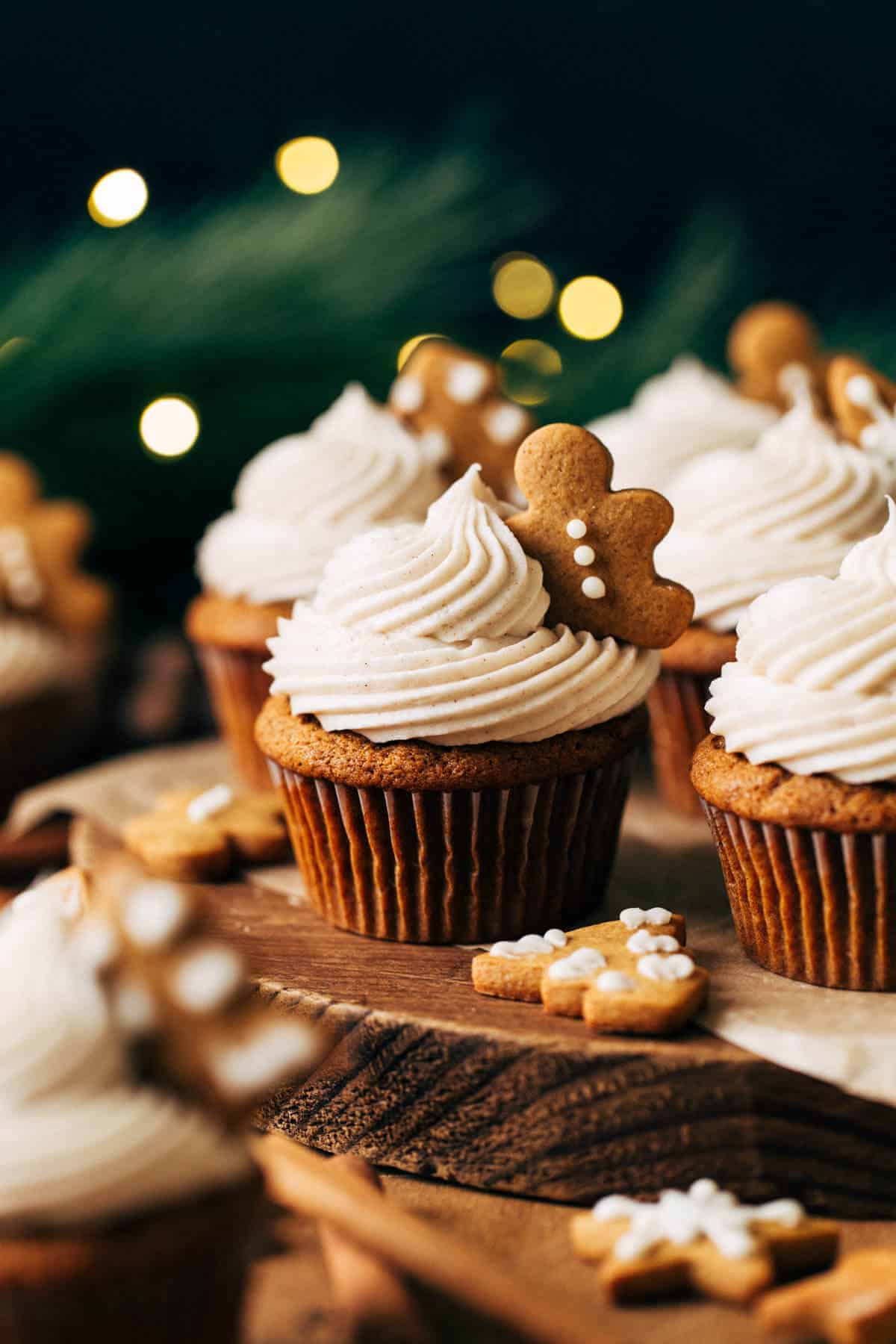 Gingerbread cupcakes on a wood slice with Christmas lights in the background.