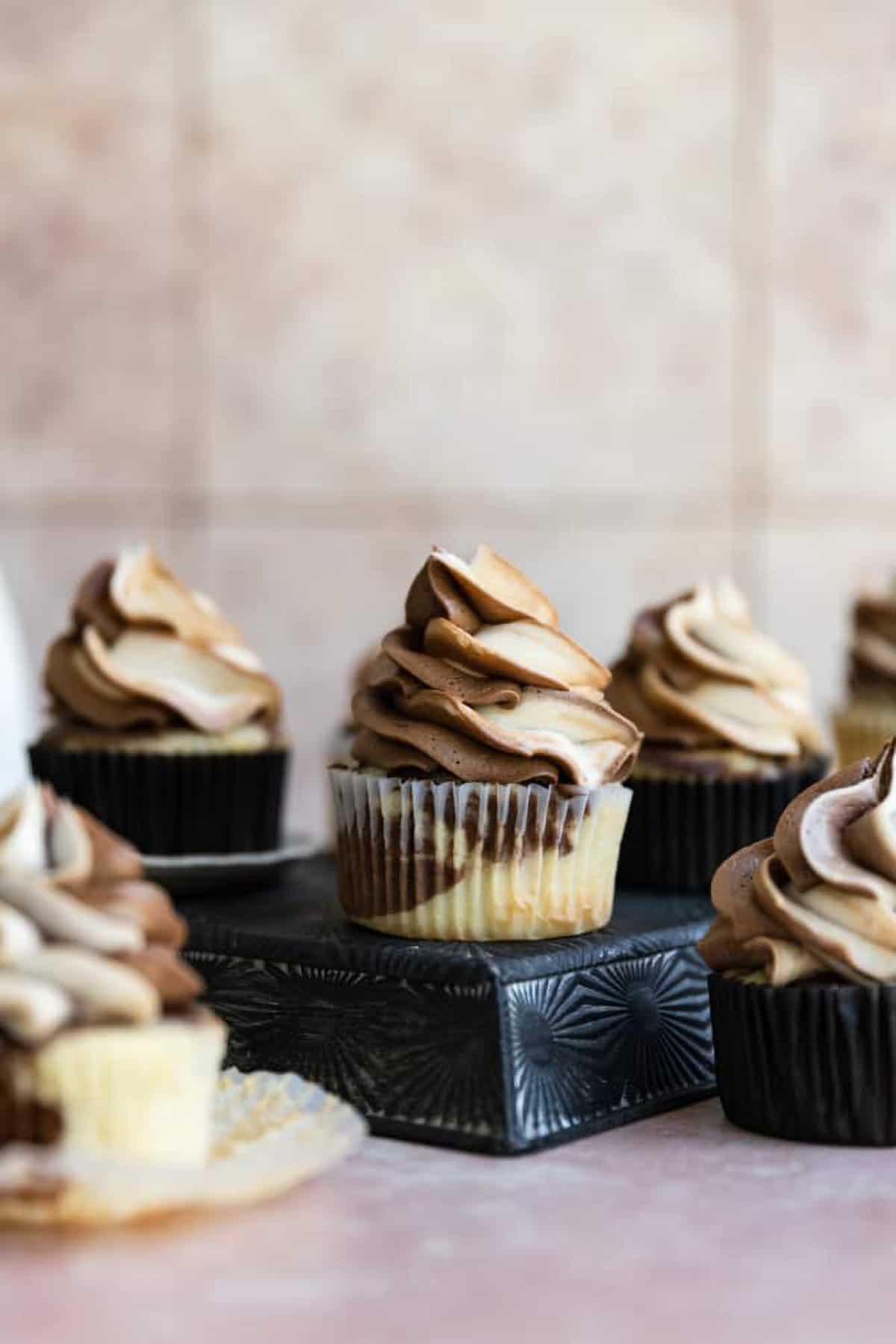 Vanilla & chocolate marble cupcakes with vanilla & chocolate marble swirled frosting on small black platform stands.