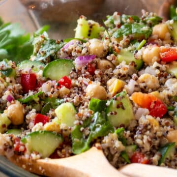Closeup of quinoa and chickpea salad with fresh vegetables in a bowl with wooden spoons.