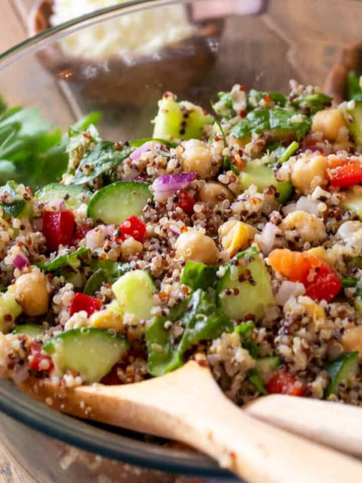 Closeup of quinoa and chickpea salad with fresh vegetables in a bowl with wooden spoons.