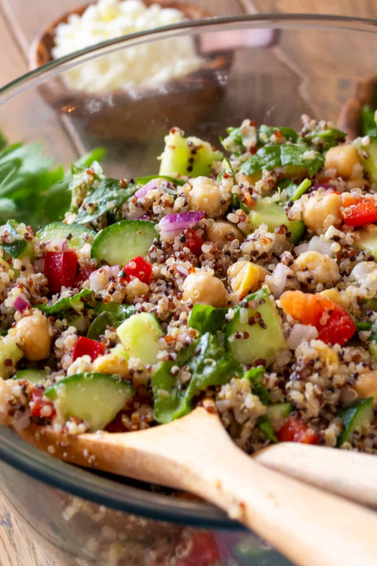 Closeup of quinoa and chickpea salad with fresh vegetables in a bowl with wooden spoons.