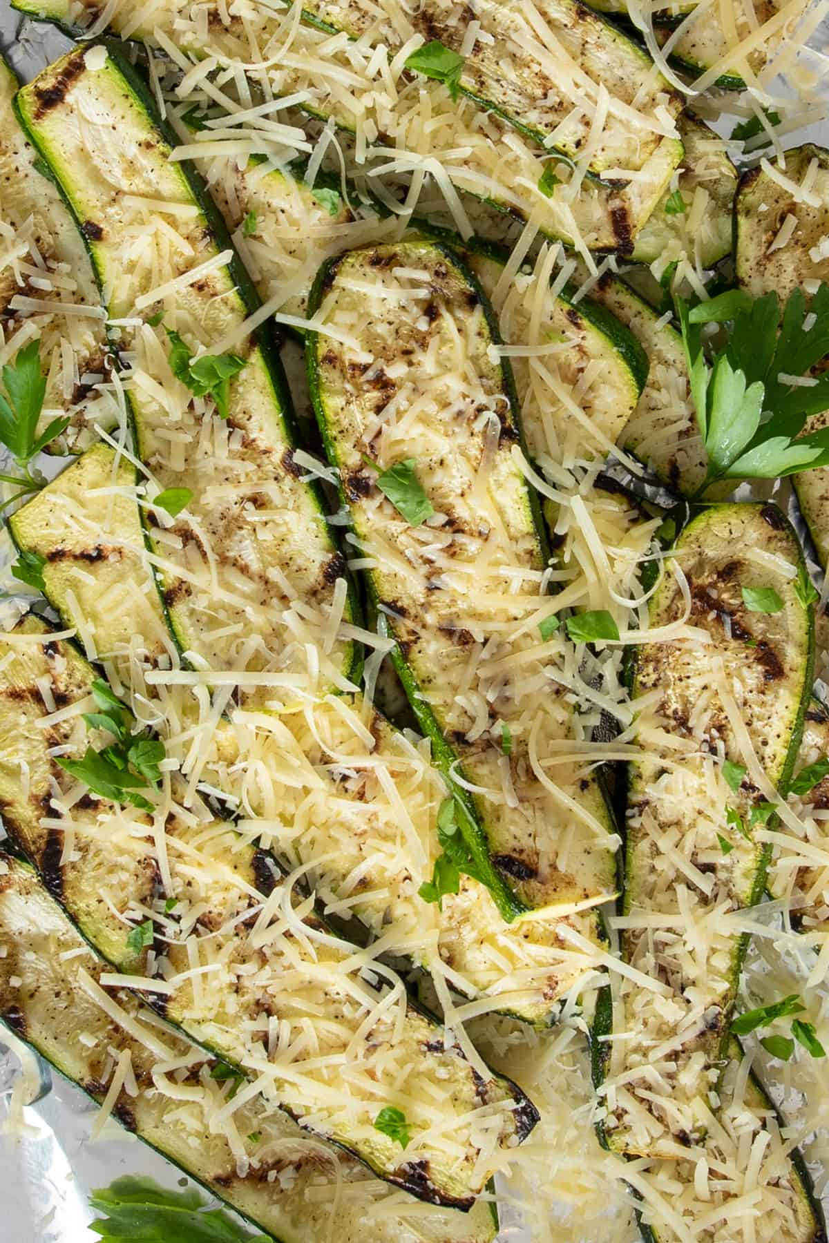 Grilled zucchini piled on foil and topped with shredded parmesan cheese.