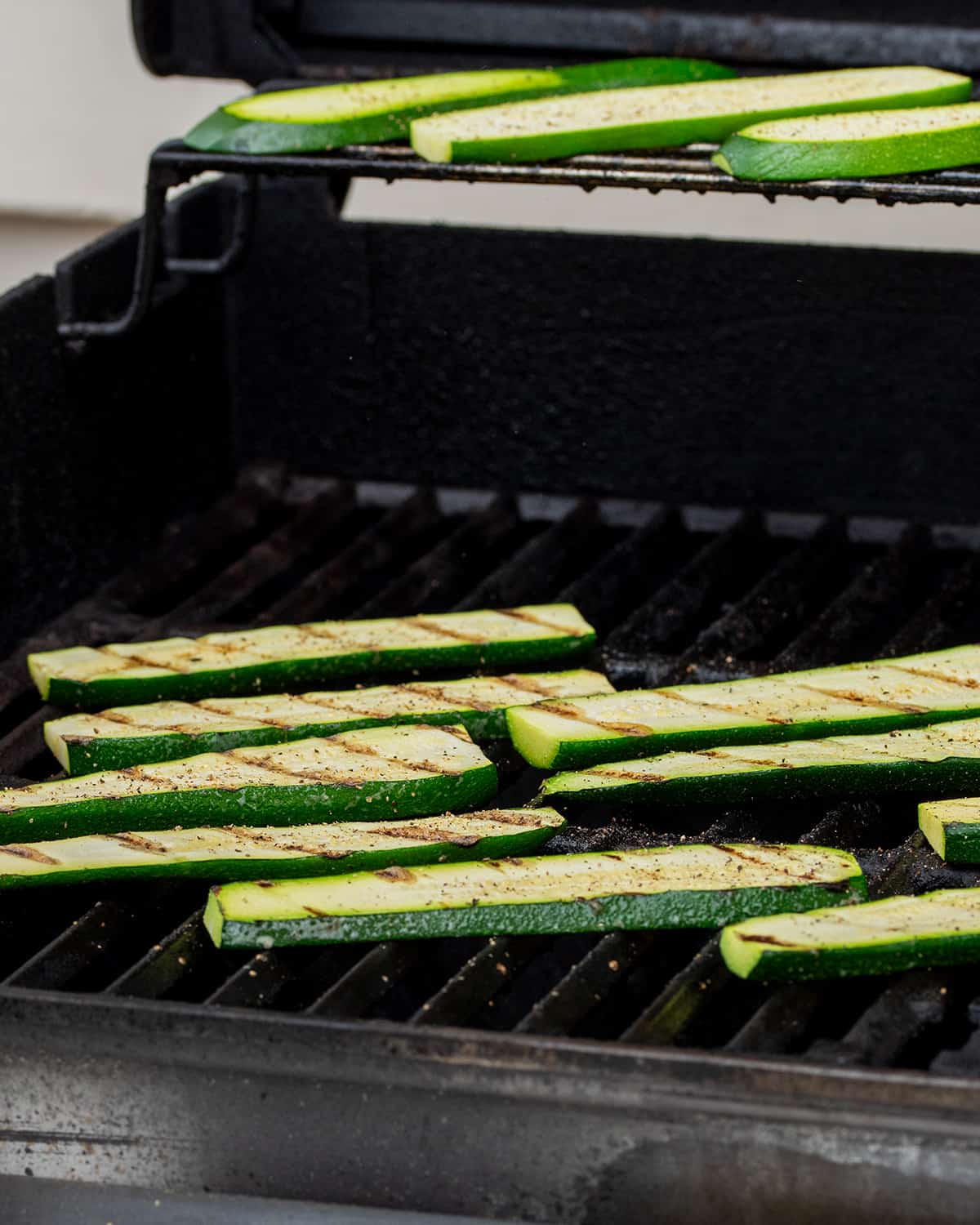 Zucchini steaks on a grill seasoned with salt and pepper.