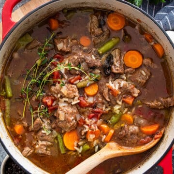 A large pot of beef and rice soup with vegetables and a wooden spoon.