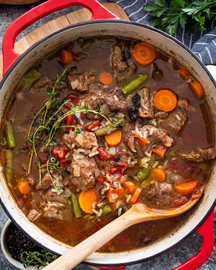 A large pot of beef and rice soup with vegetables and a wooden spoon.