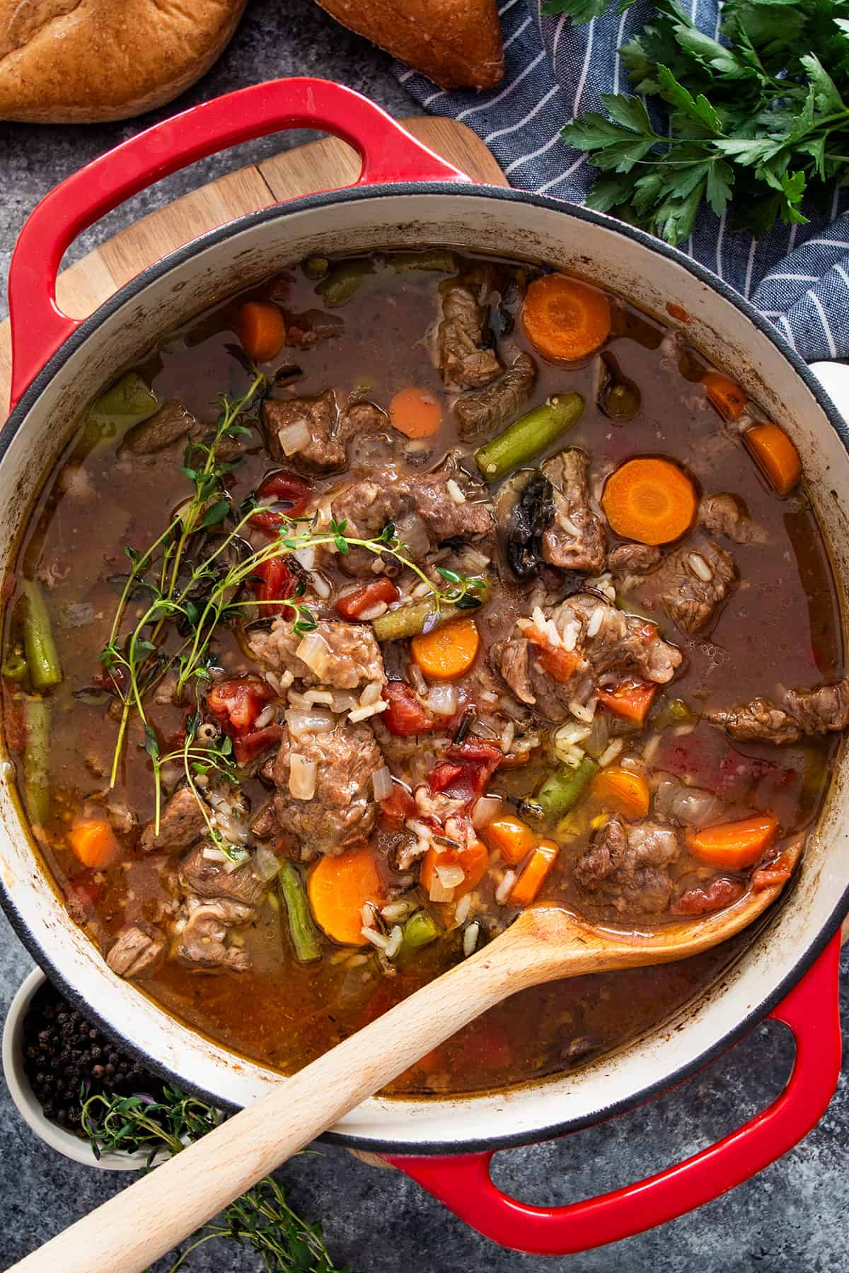 A large pot of beef and rice soup with vegetables and a wooden spoon.