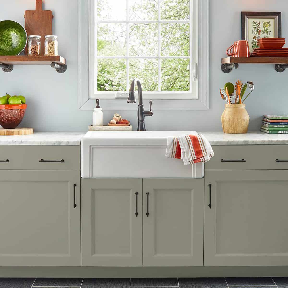 Woodland sage kitchen cabinets with marble countertops in a bright kitchen.