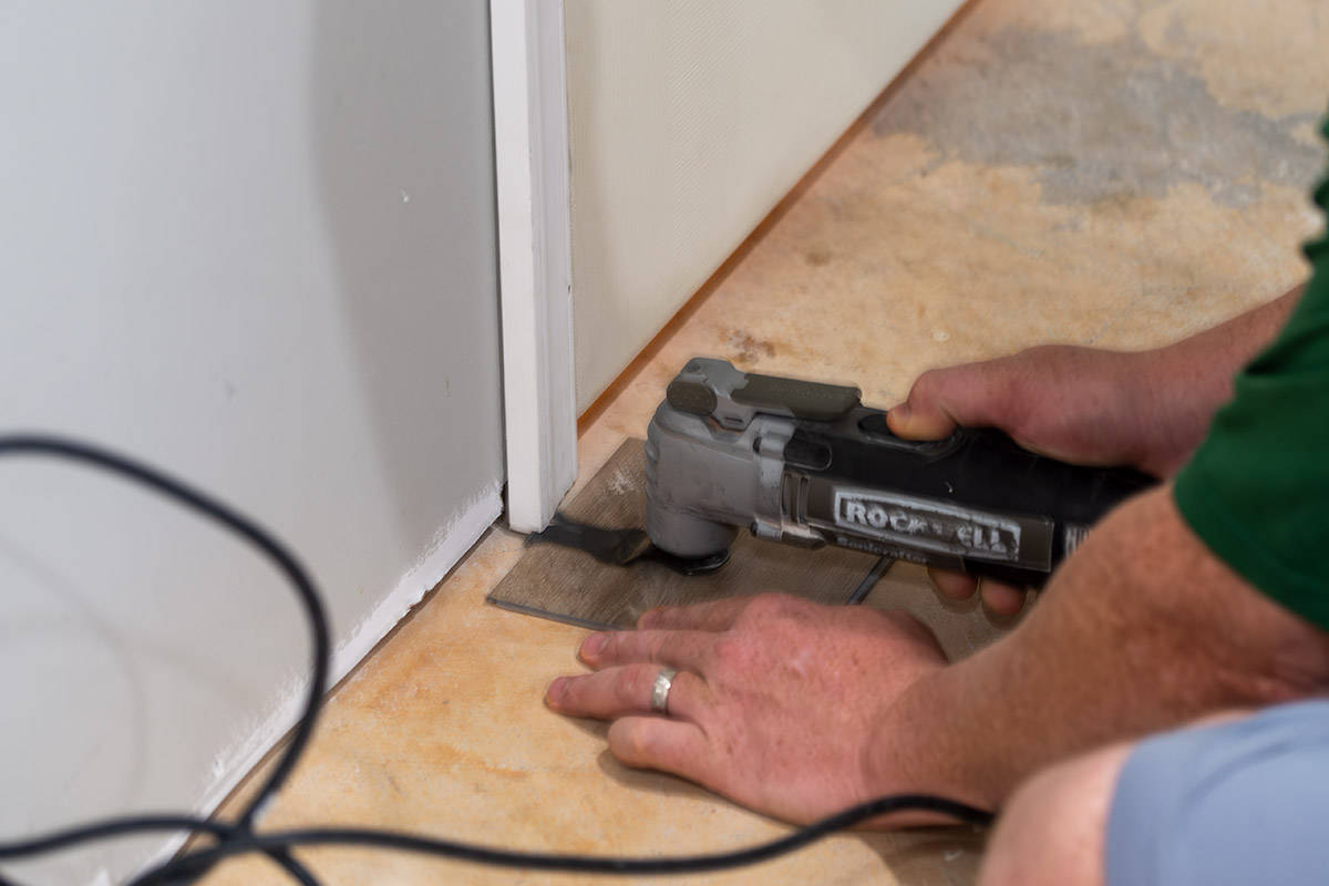 Man using a cutting tool to cut the bottom of door jambs for new floors.