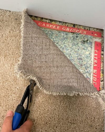 Someone using pliers to remove old carpet to show the carpet pad and strips.