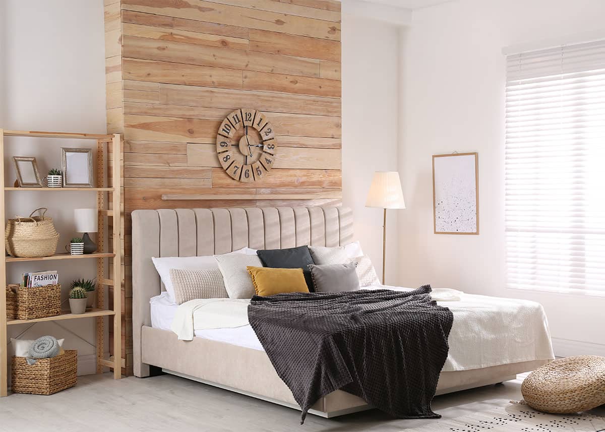 A wood feature wall behind the bed with natural slat woods and a clock.