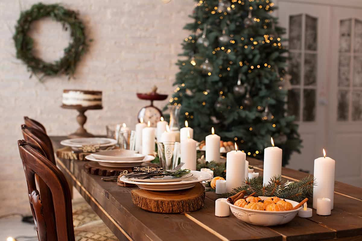 A holiday tables setting with wood tones and rustic place settings with a Christmas tree in the background.