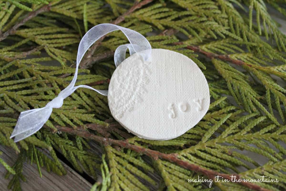 Vintage style clay Christmas tree ornaments with texture imprints of antique fabric and word stamps laced with pale blue ribbon.