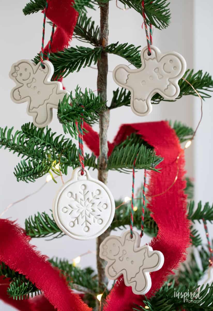 White clay cookie cutter style Christmas tree ornaments fashioned to resemble Gingerbread folk hanging from red and green string from a Charlie Brown style tree.