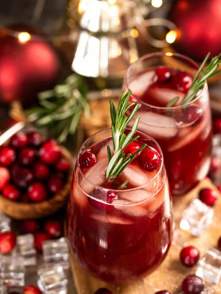 Two Glasses of Christmas punch with cranberries floating on top and a rosemary stick.