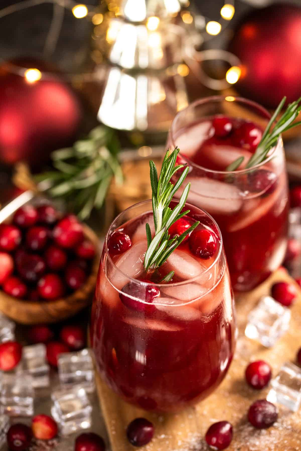 Two Glasses of Christmas punch with cranberries floating on top and a rosemary stick.