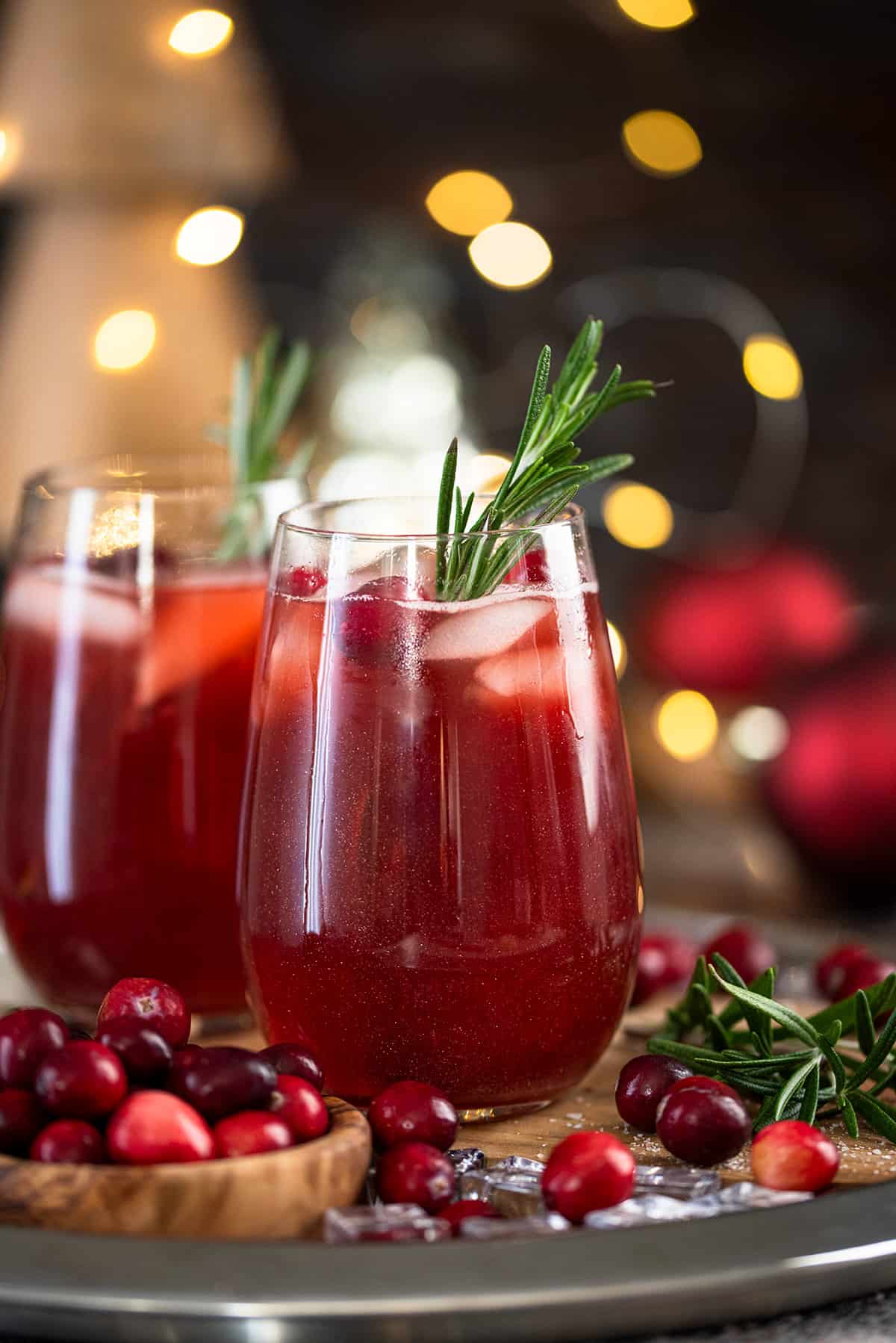 Sideview of christmas punch mocktails in wine glasses on a tray with ice and cranberries.