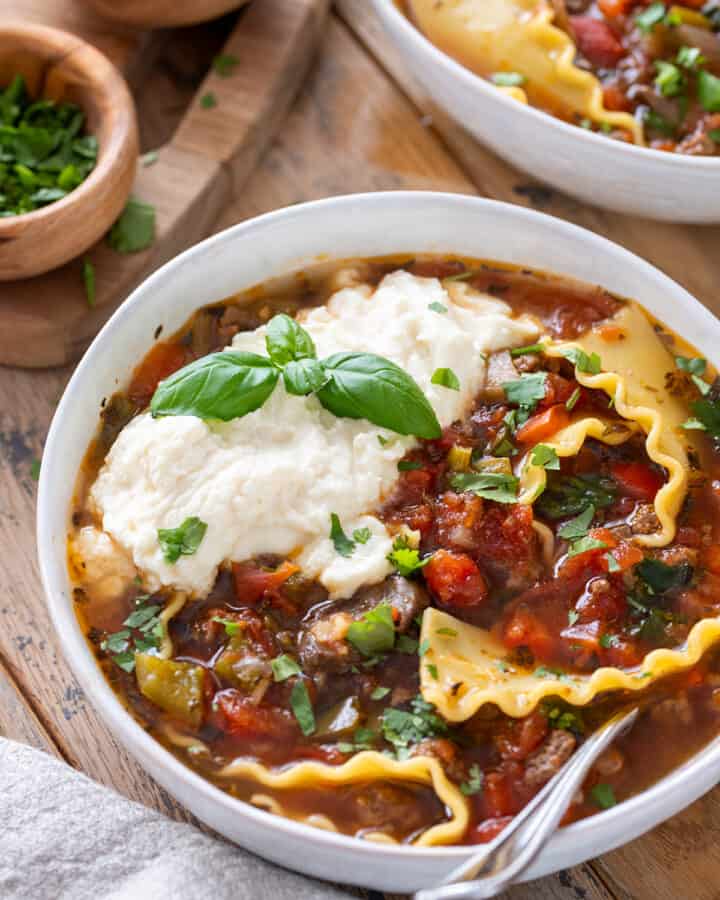 Crockpot lasagna soup in a bowl with ricotta cheese and fresh basil on top.