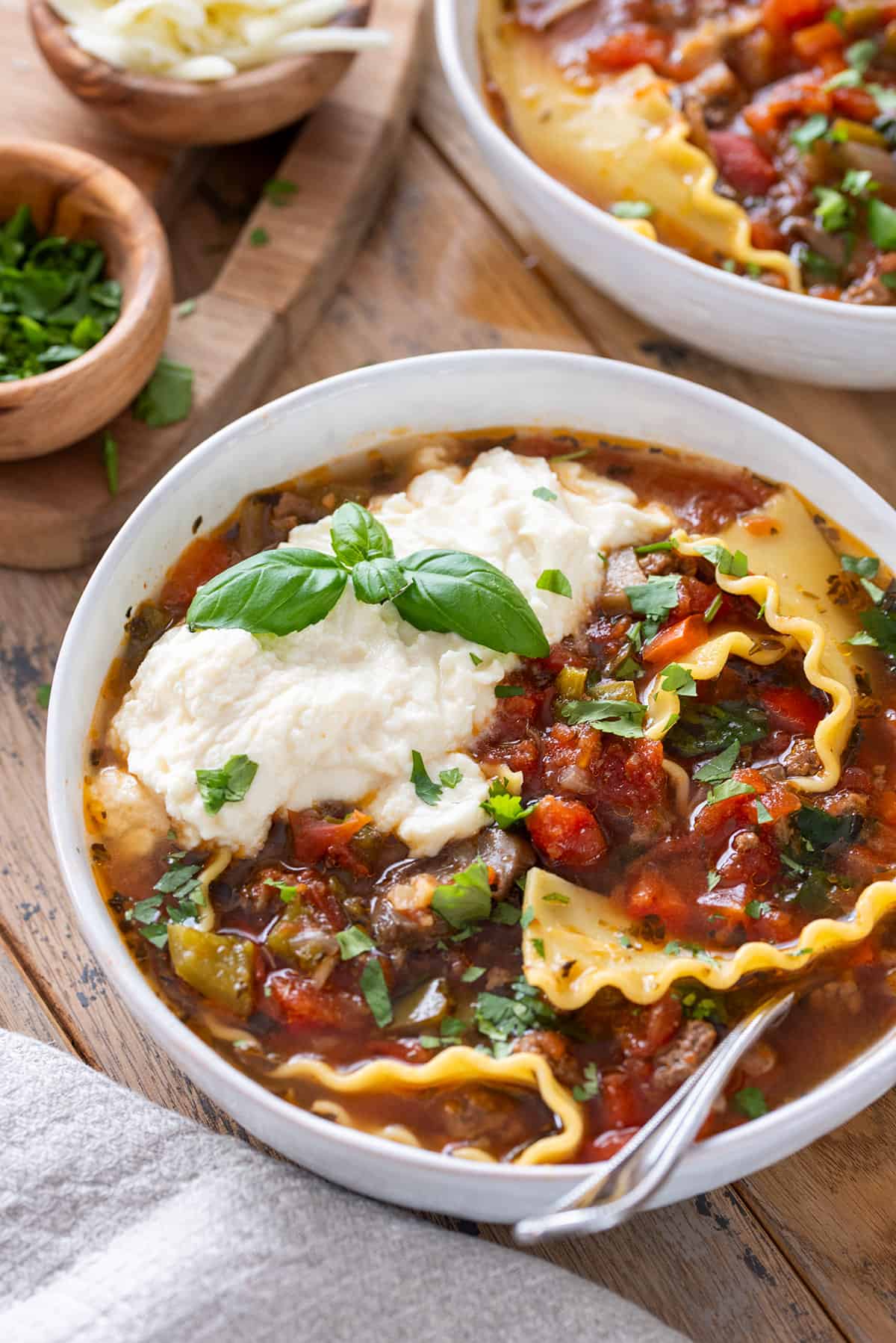 A bowl of lasagna soup with ricotta cheese and basil on top.