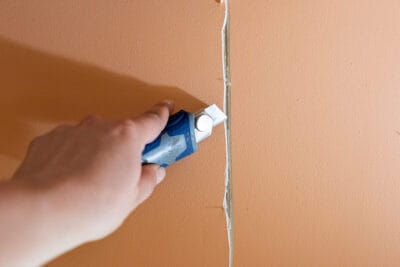 A woman cutting a v-notch around a drywall crack to fix it.