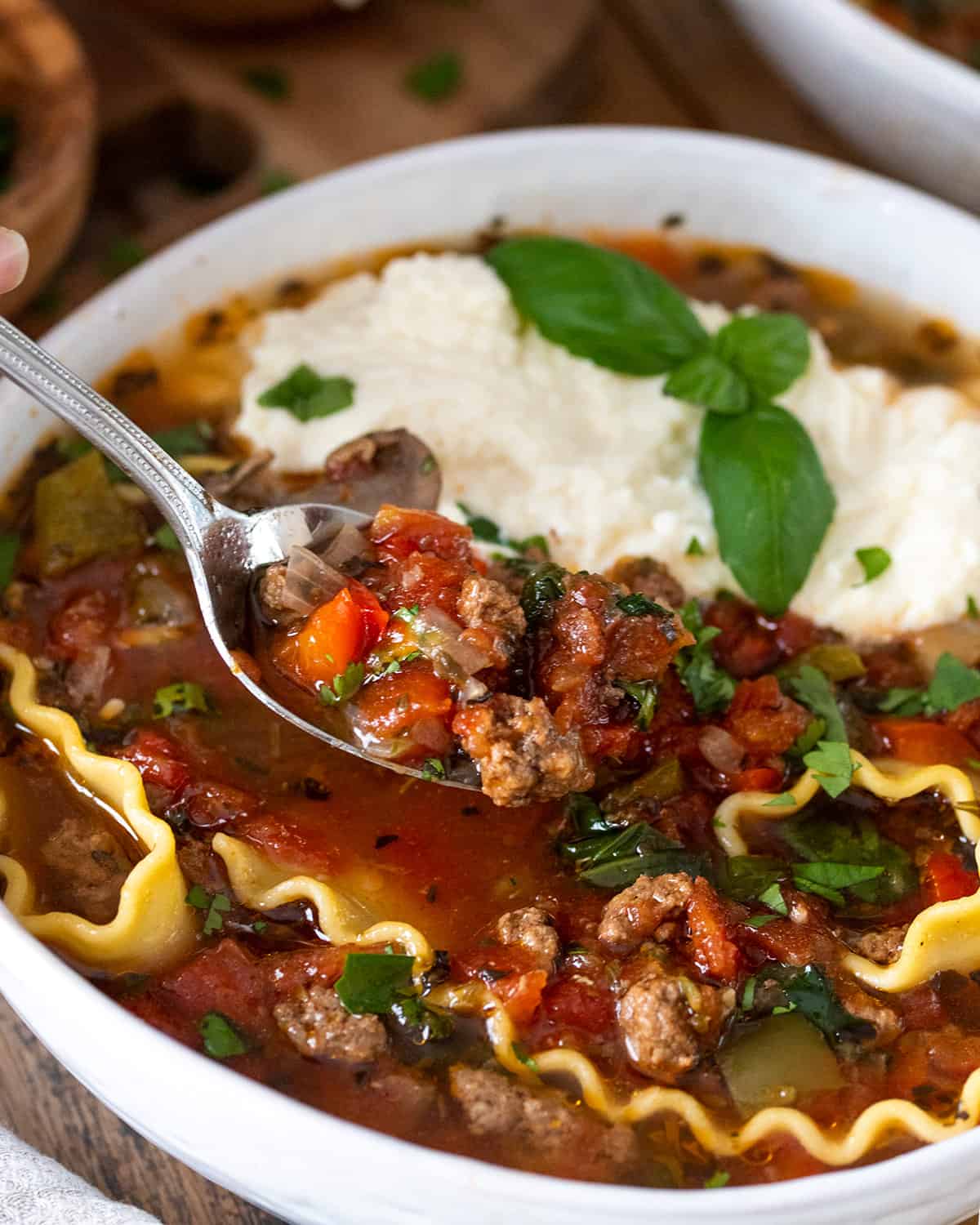 Closeup of a spoon with tomato lasagna broth on it over a bowl.