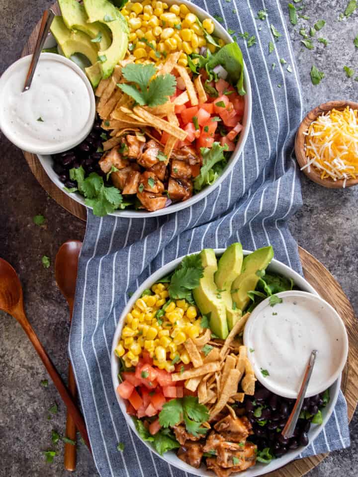Overhead of two full bowls of BBQ Chicken Salad with ranch dressing on the side.