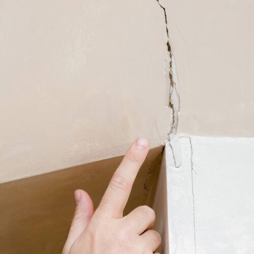 Closeup of a hand pointing to a large crack in drywall that needs fixed.