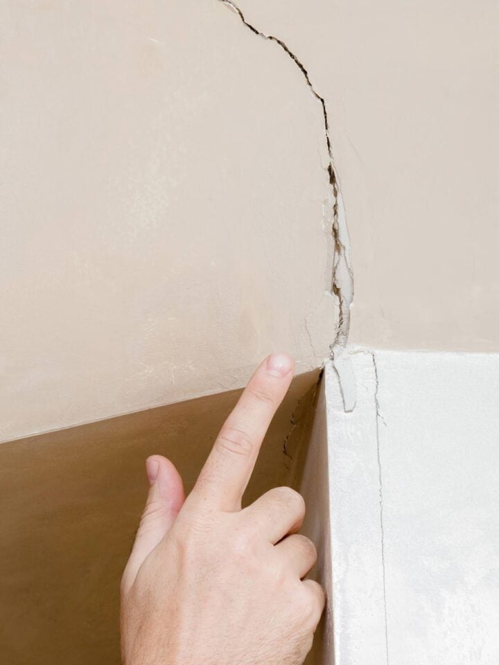 Closeup of a hand pointing to a large crack in drywall that needs fixed.