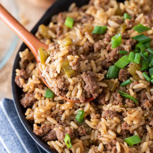 Dirty Rice in a skillet with a spoon and green onions.