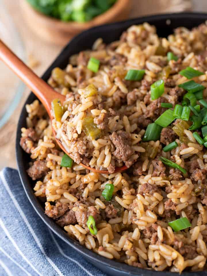 Dirty Rice in a skillet with a spoon and green onions.