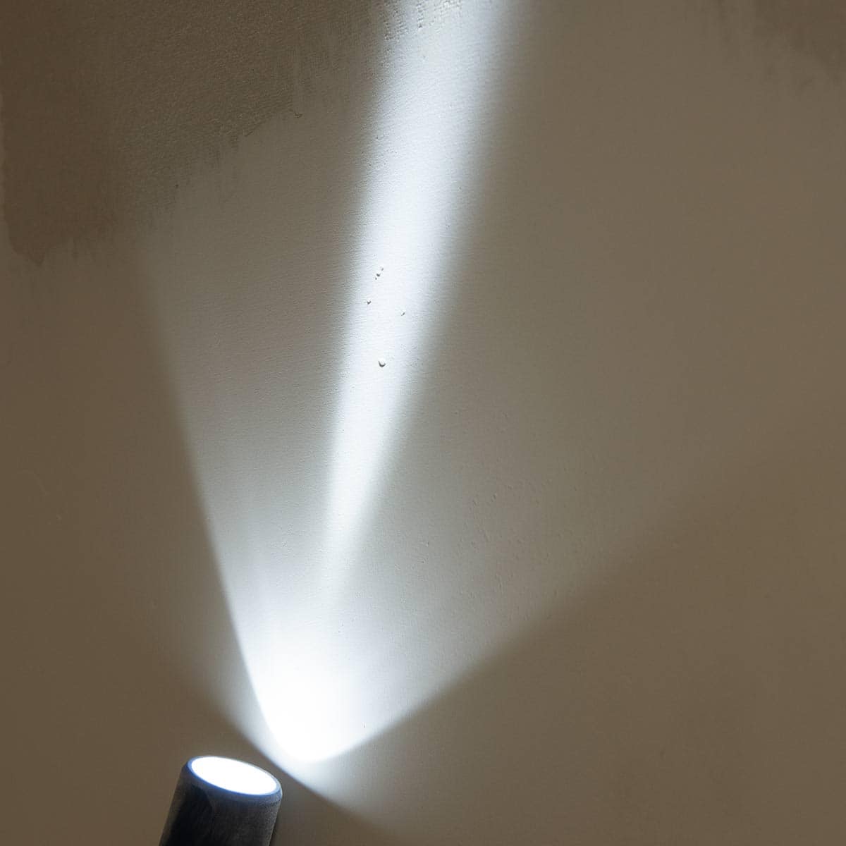 A flashlight being held up to spackle patch to reveal pin holes.
