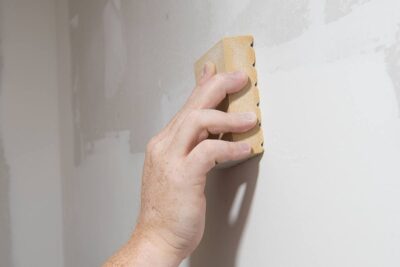 Closeup of a hand sanding drywall with a sandpaper block.
