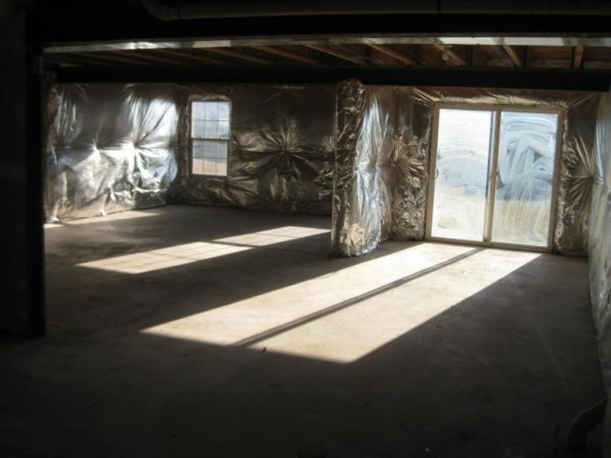 A large unfinished basement with large windows and a sliding door. Walls are covered with insulation.
