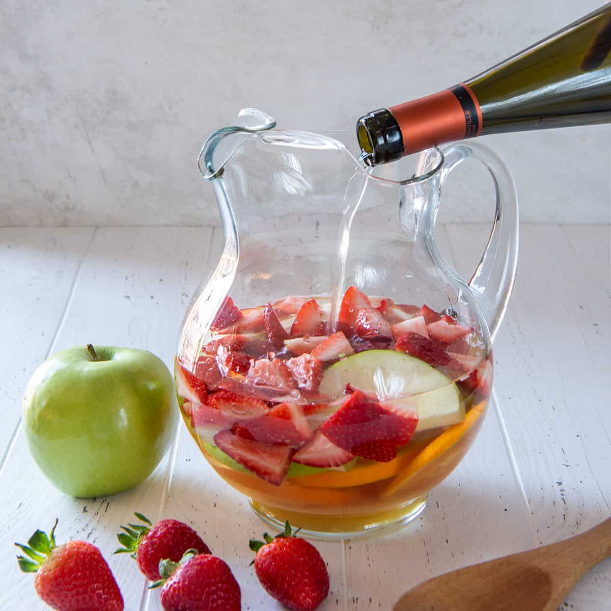 Closeup of pouring a bottle of wine into a pitcher with fruit to make white wine sangria.