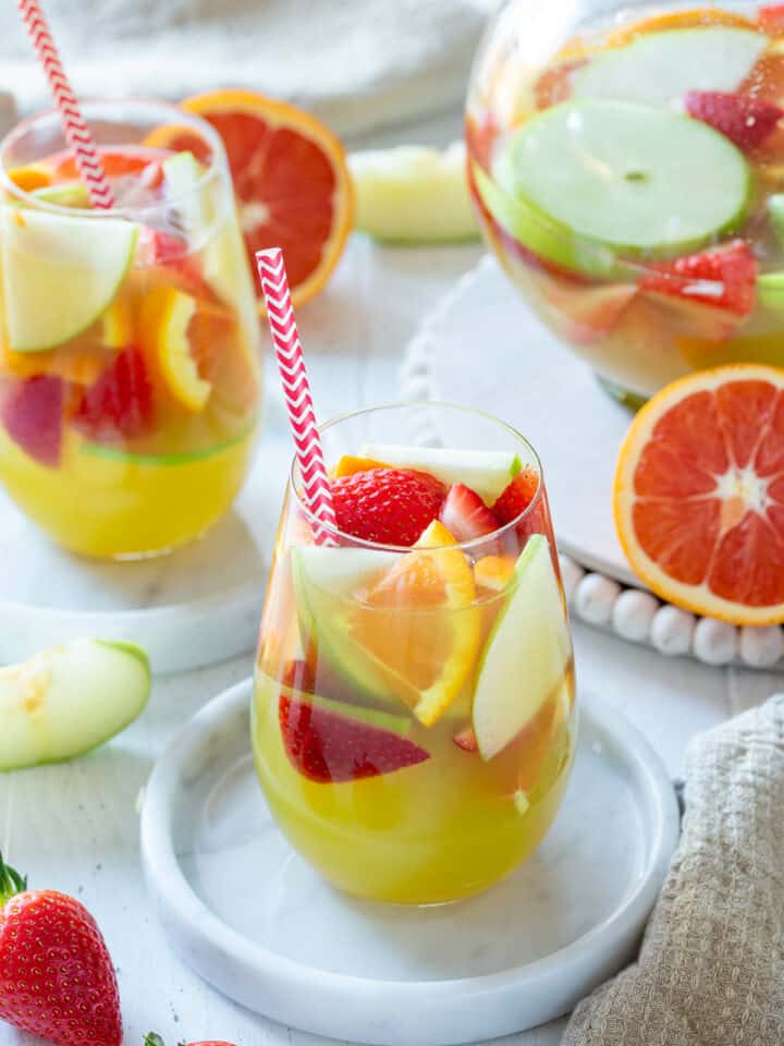 A glass of green apple sangria on marble coaster with pitcher and glasses in the background.