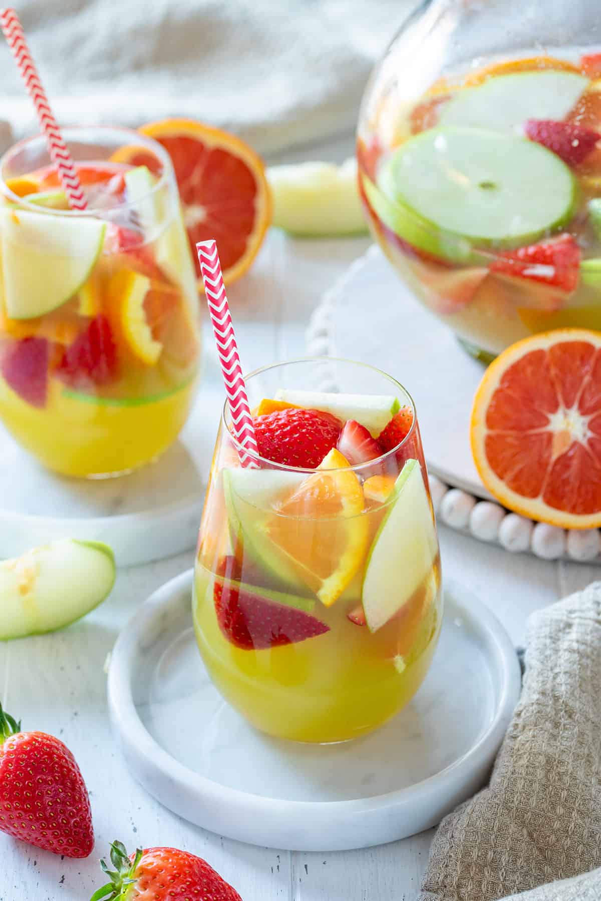 A glass of green apple sangria on marble coaster with pitcher and glasses in the background.