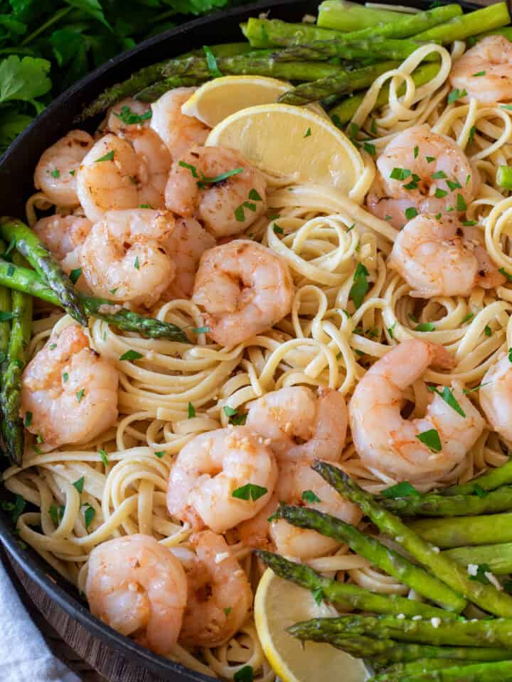 Lemon shrimp asparagus pasta in a black pan with lemon slices and parmesan cheese.