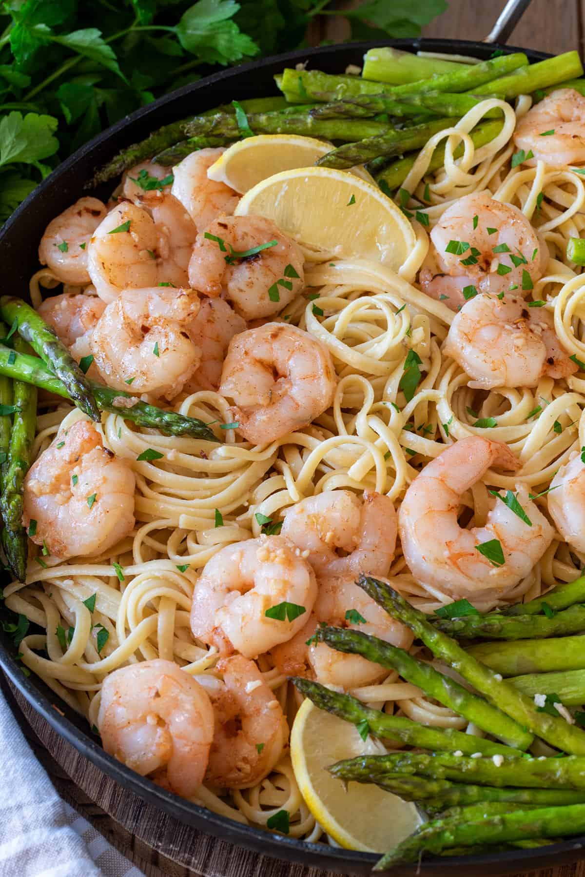 Lemon shrimp asparagus pasta in a black pan with lemon slices and parmesan cheese.