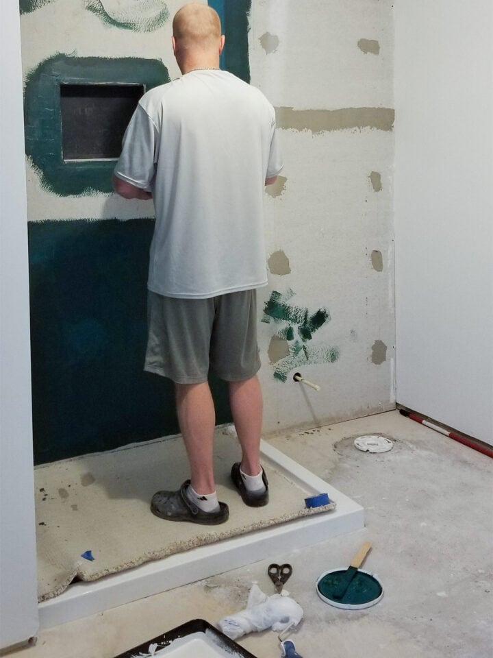 A man painting a liquid waterproofing membrane onto concrete backerboard for a shower installation.
