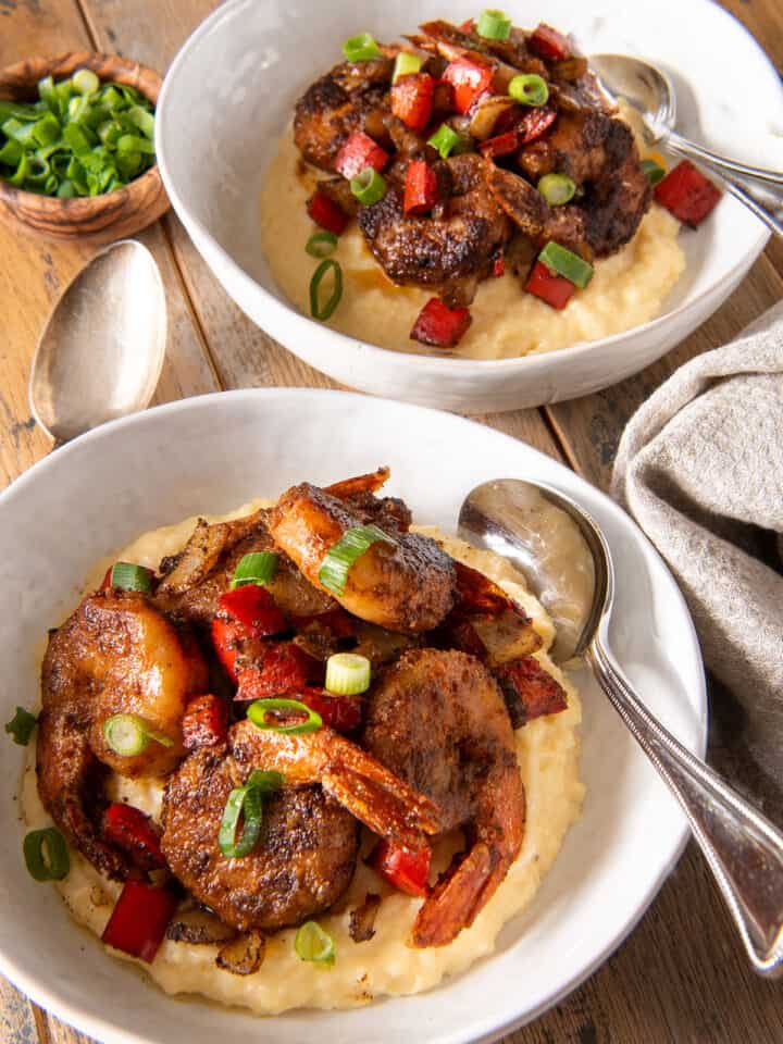 Two bowls of Cajun Shrimp and cheese grits topped with green onions and spoons.