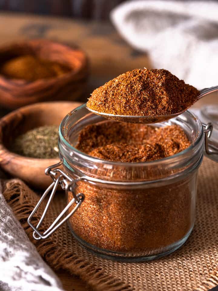 A spoonful of Cajun seasoning over top of a full spice jar.