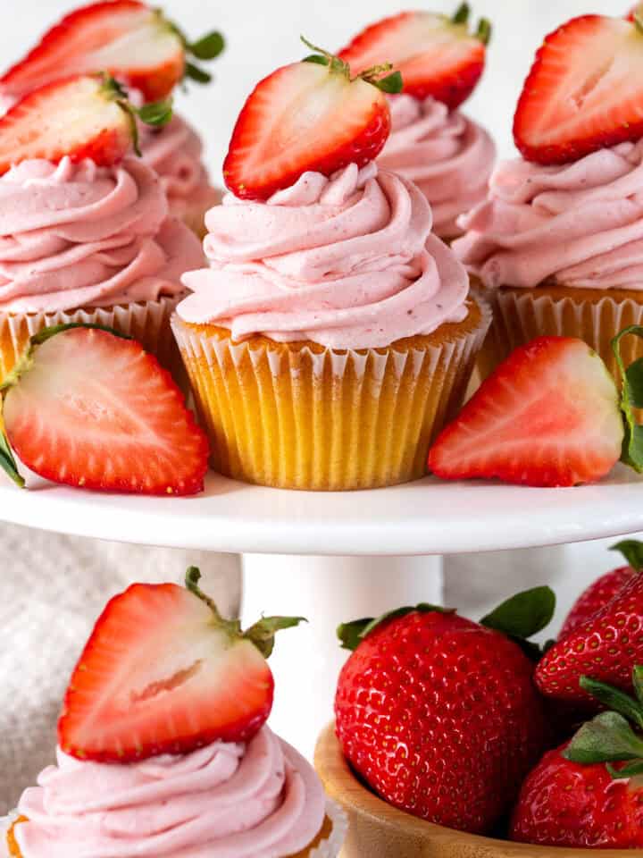 Close up of cupcake tier featuring Strawberry Cream Cheese Frosted cupcakes with fresh strawberries sliced and whole.