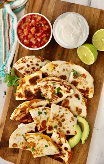 Several cheese quesadillas laid out on a platter with salsa and sour cream.