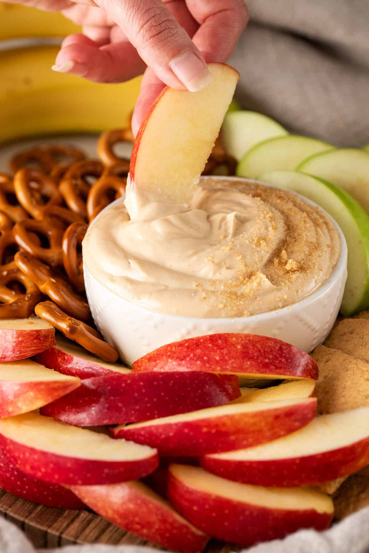 A hand dipping an apple slice into a bowl of sweet peanut butter dip.