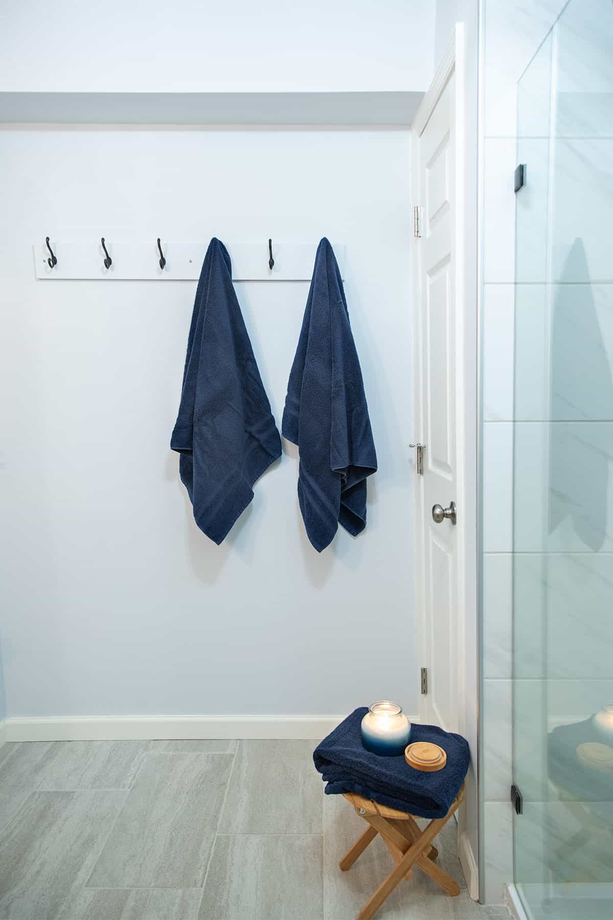 Blue bathroom with navy towel rack and a small stool to hold toiletries.