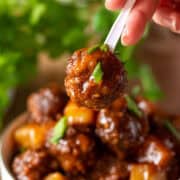 Single Hawaiian meatball on a toothpick held in front of a bowl.