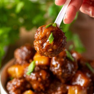 Single Hawaiian meatball on a toothpick held in front of a bowl.