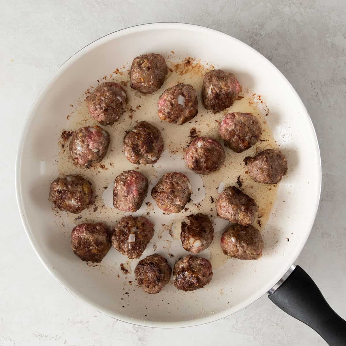 Partially cooked meatballs in a skillet.