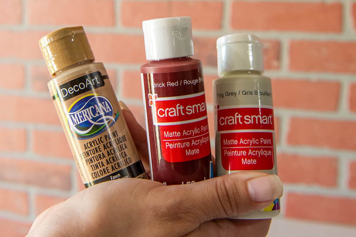 Three cans of craft paint including colors Fawn, Brick red, and fog grey to create touch up brick paint.